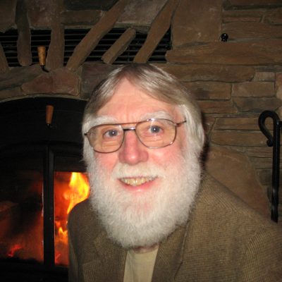 A man with a beard in front of a fireplace.