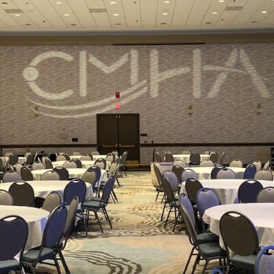 A conference room with round tables and a projected logo "cmha" on the wall.