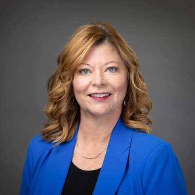 Professional woman in blue blazer smiling against a gray background.