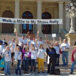 Group of individuals gathered on steps in front of a building for the "walk-a-mile in my shoes rally.