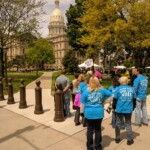 People holding signs at a demonstration near a capitol building.
