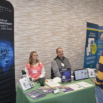 People at a booth discussing clinical treatments for anxiety, insomnia, and pain. Display of brochures and promotional materials on the table.