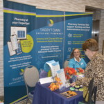 A person visits an informational pharmacy booth with two banners promoting services and products at an event.