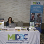 A woman sitting at a booth for the Michigan Developmental Disabilities Council, with brochures and informational banners displayed.