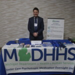 A man stands behind a table displaying informational materials and a banner for the Michigan Department of Health and Human Services at an event.
