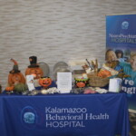 Display table with Halloween-themed decorations, informational brochures, and a Kalamazoo Behavioral Health Hospital banner in a conference setting.