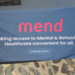 A tablecloth with the word "mend" and the slogan "Making access to Mental & Behavioral Healthcare convenient for all." The website "mend.com" is also displayed.
