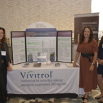 Three people standing beside a Vivitrol information booth.