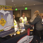 People interacting at a booth with a "Work Zone" sign, featuring a map and construction imagery, at an indoor event.