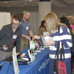 People at a conference booth, interacting with displays and brochures at a table.