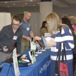 People at a conference booth, interacting with displays and brochures at a table.
