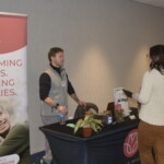 Person at an information booth with a "Reclaiming Lives. Healing Families." banner talks to a visitor in a hallway setting.